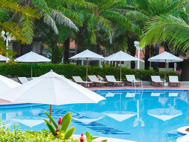 Área de piscina al aire libre con tumbonas y sombrillas blancas rodeada de vegetación tropical.