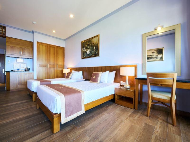 Habitación de hotel luminosa con dos camas individuales, muebles de madera y cocina al fondo.