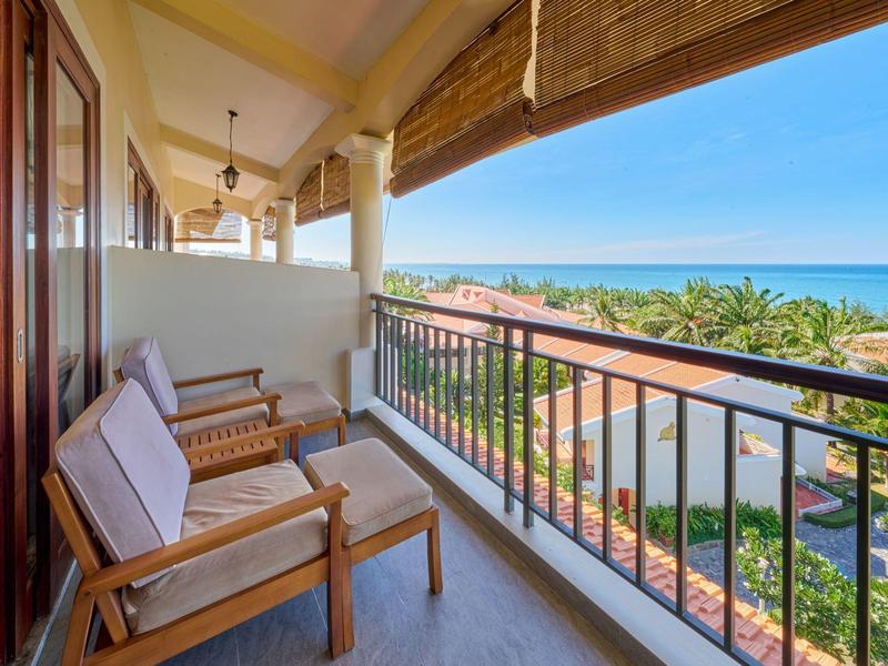 Balcón con muebles de madera y vista a vegetación tropical y el mar a lo lejos.