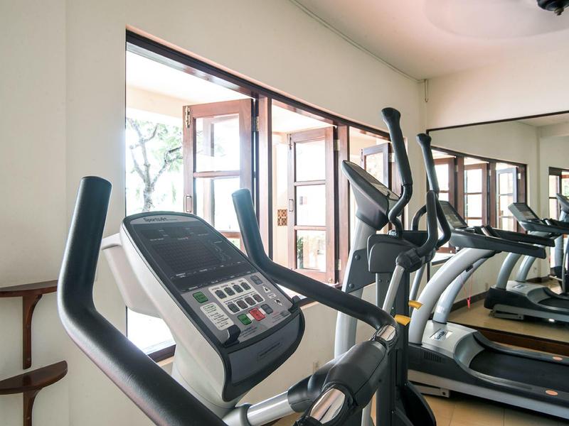 Gimnasio moderno con cinta de correr y entrenador elíptico frente a grandes ventanas y pared de espejos.
