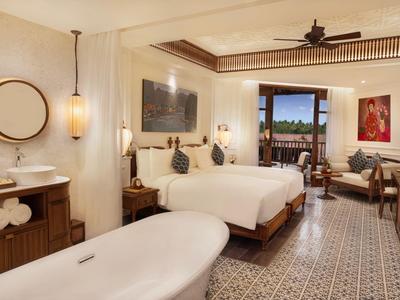 Helles Schlafzimmer mit zwei Betten, Badewanne, Holzmöbeln und Zugang zu Balkon mit Blick ins Grüne.