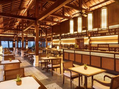 Großes Restaurant mit Holzdach, hölzernen Tischen und Stühlen, warmem Licht und Pflanzen auf den Tischen.