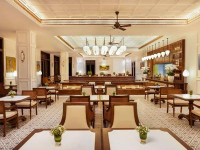 Großes helles Restaurant mit rechteckigen Tischen, Holzmöbeln und Deckenventilator.