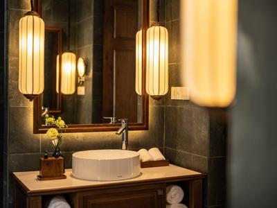 Modernes Badezimmer mit rundem Waschbecken, Holzmöbel und warmen, vertikalen Hängeleuchten.