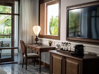 Gemütlicher Raum mit Holzmöbeln, Schreibtisch, Stuhl, Lampe, Fernseher und Fensterblick auf Grün.