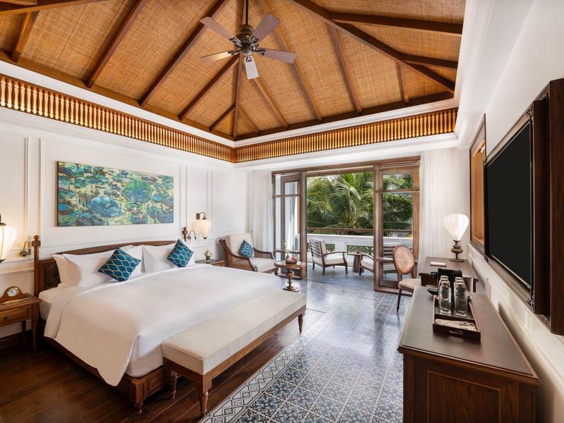 Geräumiges Schlafzimmer mit Holzbett, Ventilator, Fernseher und Balkon mit grünem Ausblick.