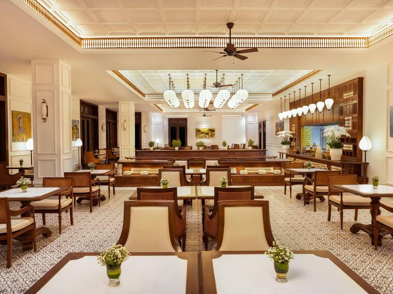 Großes helles Restaurant mit rechteckigen Tischen, Holzmöbeln und Deckenventilator.