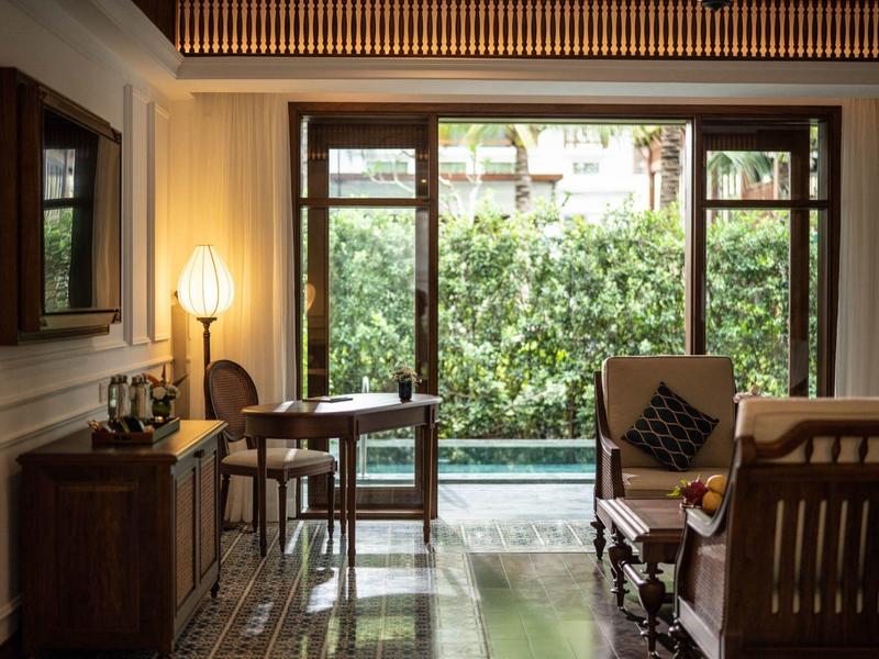 Gemütliches Wohnzimmer mit Holzmöbeln, Glasfenstern und Blick auf grünen Garten mit Pool.