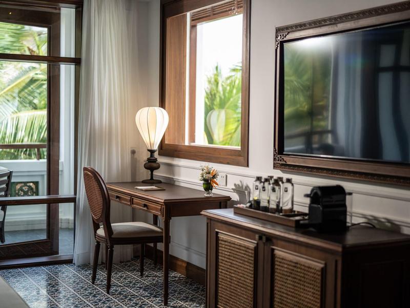 Gemütlicher Raum mit Holzmöbeln, Schreibtisch, Stuhl, Lampe, Fernseher und Fensterblick auf Grün.