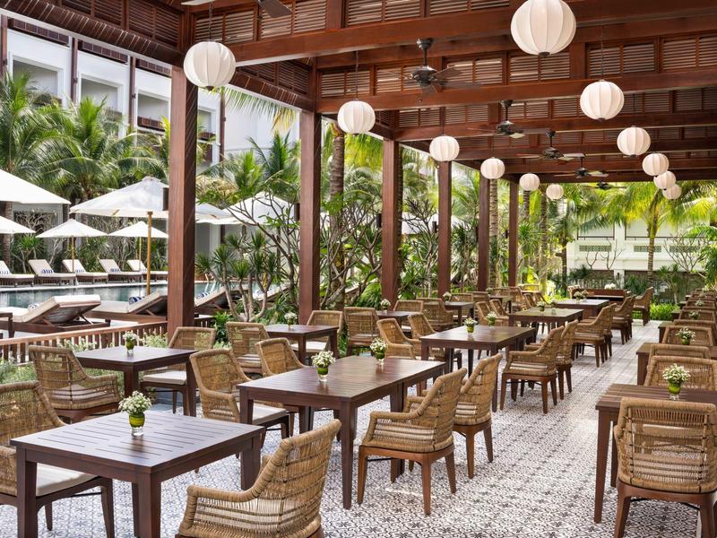 Gemütliche Terrasse mit Holzmöbeln, weißen Lampen und Blick auf Pool und Pflanzen.