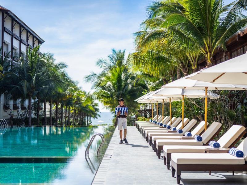 Luxuriöser Poolbereich mit Liegestühlen, Sonnenschirmen und Palmen an einem sonnigen Tag.