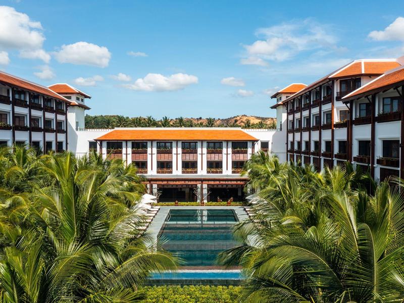 Luxushotel mit roten Dächern, großen Pools und Palmen unter blauem Himmel.