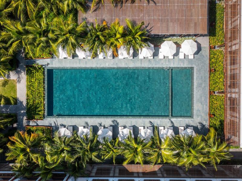 Rechteckiger Pool inmitten von Palmen, umgeben von Liegestühlen und weißen Sonnenschirmen.