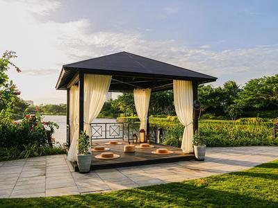 Moderner Pavillon mit Vorhängen und Sitzkissen im Garten bei Sonnenuntergang.