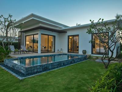 Moderní dům s bazénem a upravenou zahradou pod jasnou oblohou.
