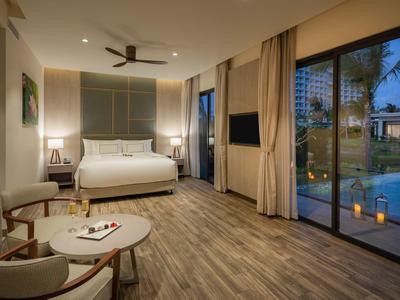 Moderní hotelový pokoj s manželskou postelí, terasou a osvětleným bazénem v noci.