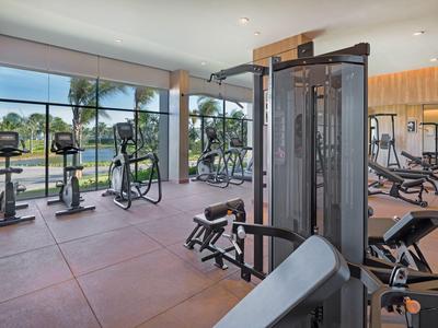 Helles Fitnessstudio mit modernen Geräten und großen Fenstern mit Blick auf Grünflächen.