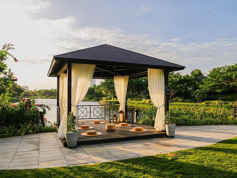 Pergola s lehkými závěsy, polštáři a rostlinami u zelené zahrady.