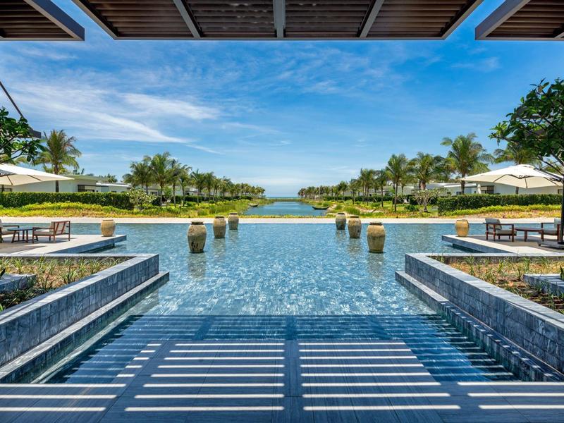 Luxusní bazén s lehátky a slunečníky, výhled na moře pod modrou oblohou.