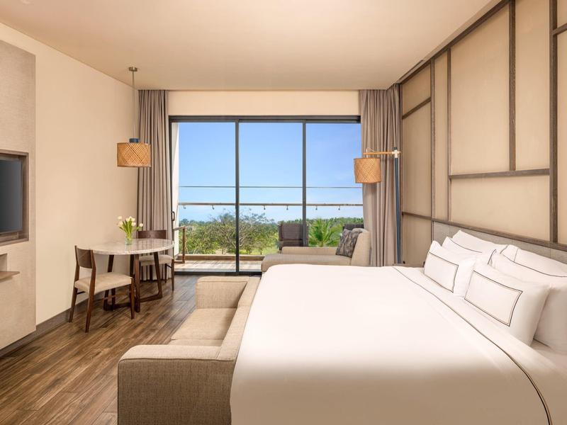 Moderní hotelový pokoj s velkou postelí, psacím stolem a výhledem na přírodu oknem.