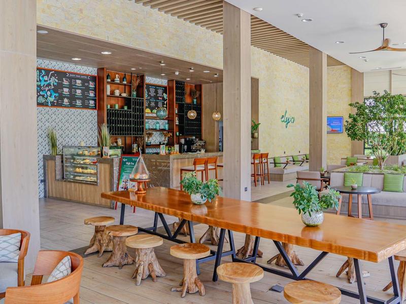 Interiér moderní kavárny s velkými dřevěnými stoly a světlým uspořádáním.