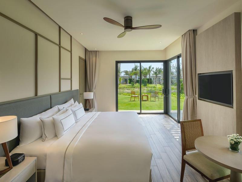 Moderní hotelový pokoj s velkou postelí, lampami, televizí a výhledem do zahrady.