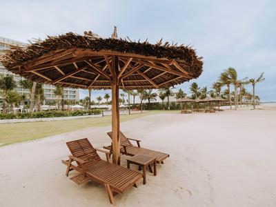 Houten ligbedden onder een strooien parasol op het strand met hotel op de achtergrond