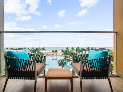 Deux fauteuils confortables avec coussins bleus sur un balcon surplombant une piscine et des palmiers.