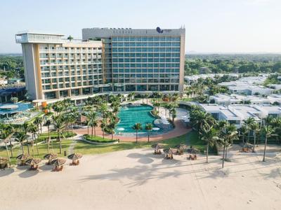 Luxe hotel met groot zwembad en palmbomen direct aan het zandstrand onder heldere lucht.