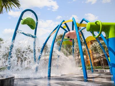Kleurrijke waterspeeltuin met waterspatbogen en fonteinen onder een blauwe hemel.
