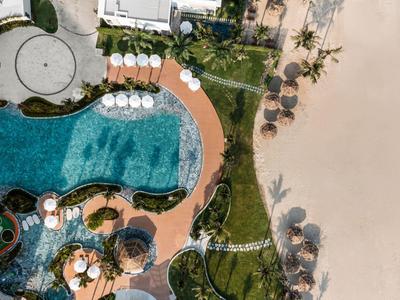 Dronezicht op een hotel met zwembad, ligstoelen, gazons en zandstrand.