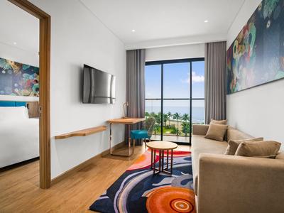 Moderne hotelkamer met bank, bureau, tv aan de muur en uitzicht op zwembad en tuin.