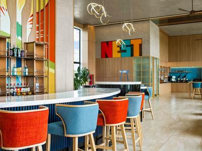 Lichte hotelbar met kleurrijke stoelen en decoratieve wandplanken.