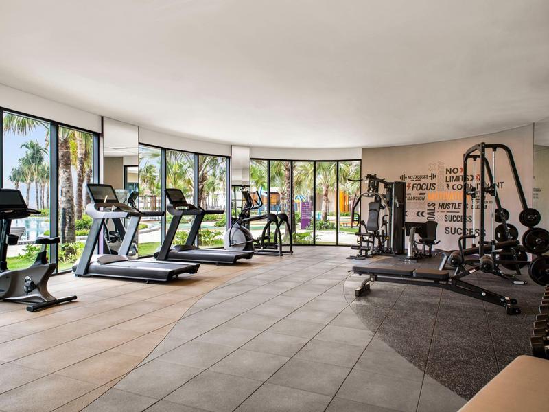 Lichte hotelgym met loopbanden, crosstrainers en krachtapparatuur, omringd door grote ramen.