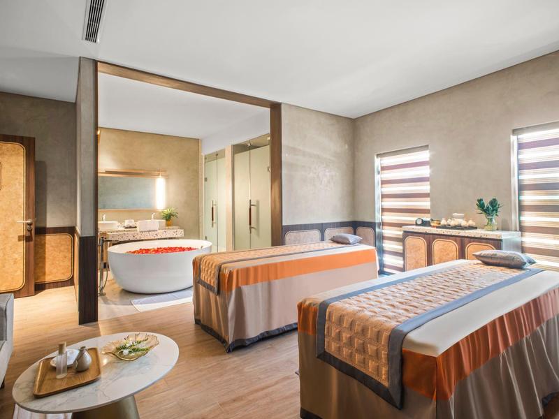 Lichte massageruimte met twee tafels, een bijzettafel en uitzicht op de badkamer.