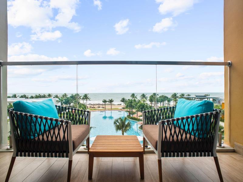 Balkon met twee stoelen en tafel met uitzicht op zwembad en zee op de achtergrond.