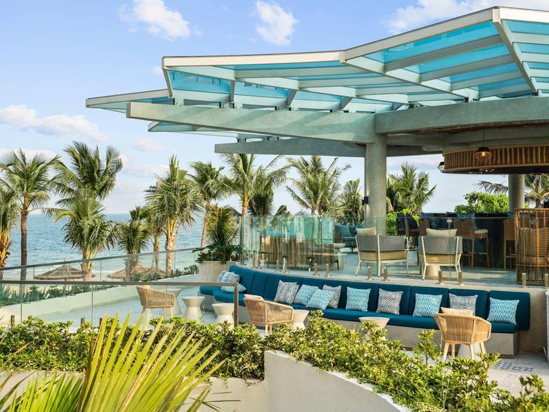 Moderne buitenruimte met bar, loungeset en zeezicht, omgeven door palmbomen en planten.