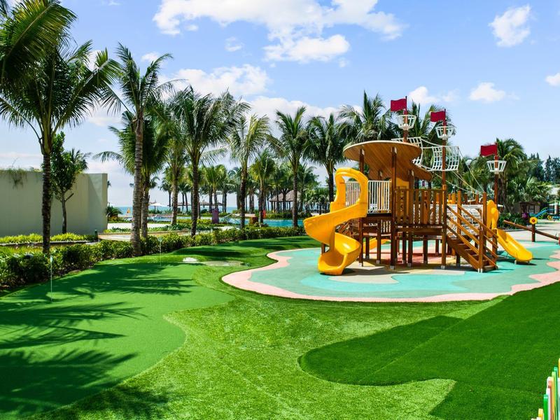 Kinderspeeltuin met glijbanen en klimrek naast palmbomen in een hoteltuin.