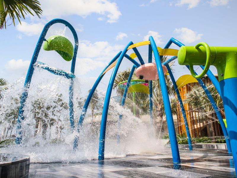 Kleurrijke waterspeeltuin met waterspatbogen en fonteinen onder een blauwe hemel.