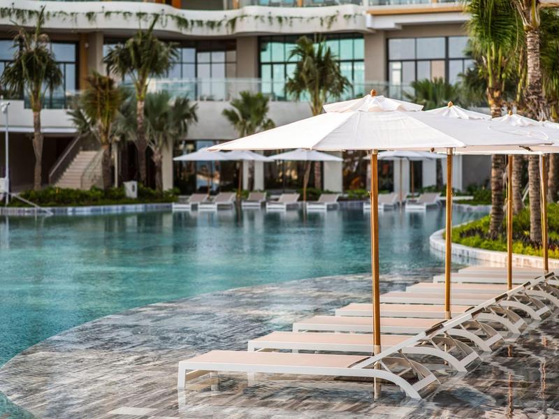 Modern hotelzwembad met ligstoelen en parasols in een tropische omgeving