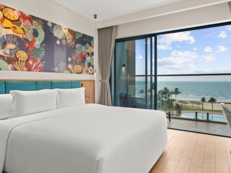 Helder verlichte hotelkamer met groot bed en balkon met uitzicht op zee.