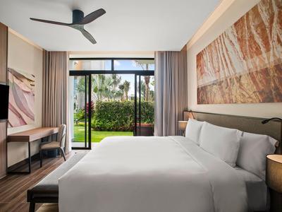 Nowoczesny pokój hotelowy z dużym łóżkiem, obrazem na ścianie i widokiem na ogród przez szklane okna.