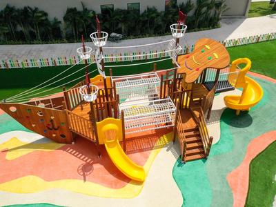 Kolorowy plac zabaw w kształcie statku z zjeżdżalniami i siatkami do wspinaczki na miękkiej nawierzchni.