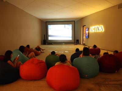 Persone sedute su pouf guardano un film in una piccola sala proiezioni.