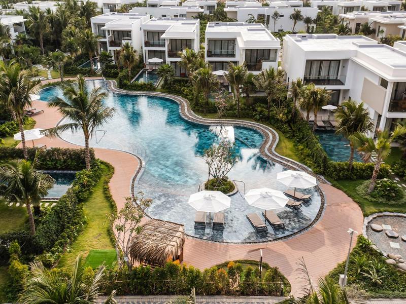 Luksusowe wille z zakrzywionym basenem otoczonym palmami i parasolami.