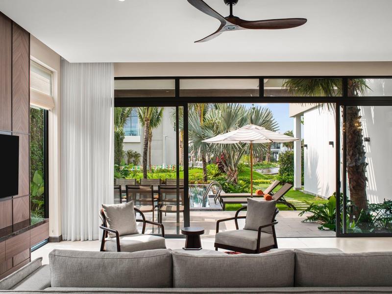 Nowoczesny salon z dużymi szklanymi oknami z widokiem na ogród z miejscami do siedzenia i parasolem.