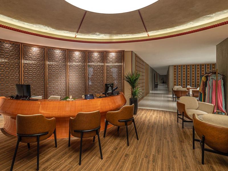 Nowoczesna recepcja z okrągłym wooden biurkiem i brązowymi krzesłami w ciepło oświetlonym pomieszczeniu.