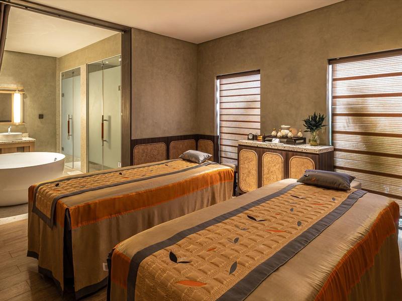 Przytulny pokój do masażu z dwoma leżankami i ciepłym, stonowanym oświetleniem.