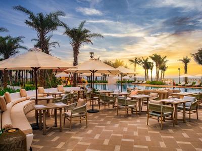 Outdoor resort area with tables, umbrellas, and palm trees at sunset