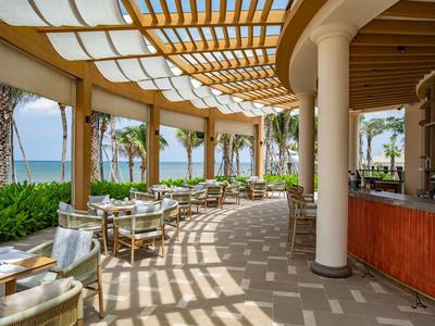 Terrazza coperta con sedie e tavoli, vista su palme e mare.